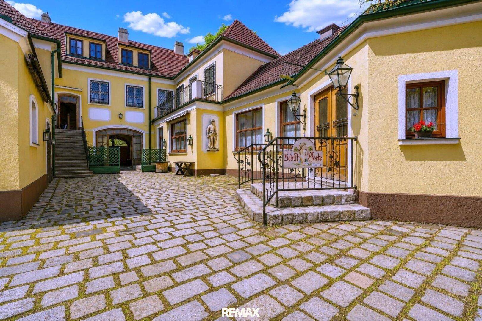 Historischer Innenhof mit Kopfsteinpflaster, umgeben von traditionellen gelben Gebäuden und Außentreppen.