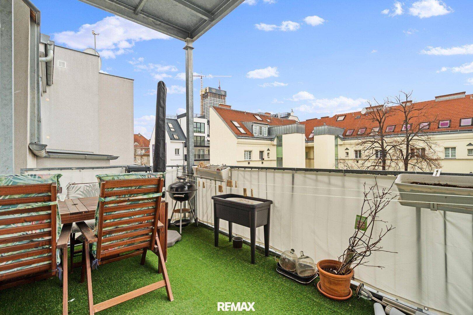 Möblierter Balkon mit Kunstrasen, Grill und Blick auf die Stadt.