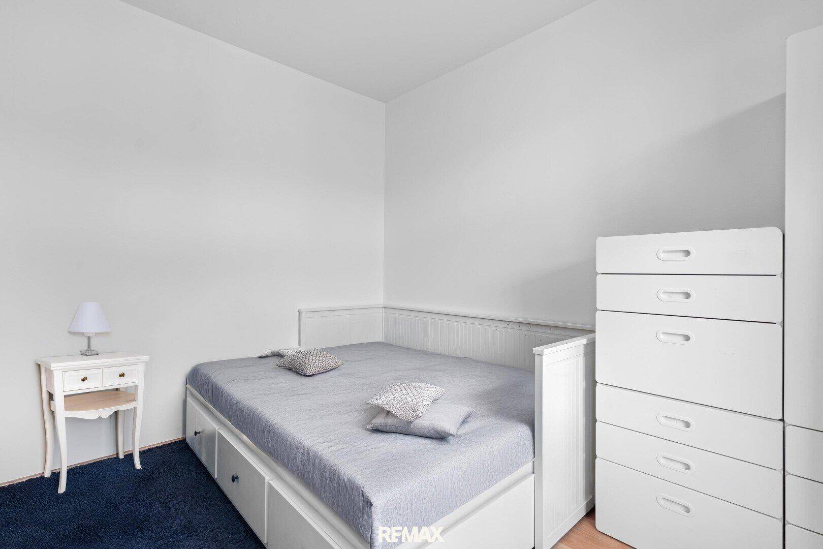 Kleines Schlafzimmer mit Einzelbett, weißer Kommode und blauem Teppich.