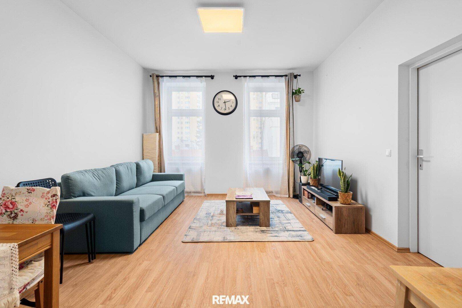 Einfaches Wohnzimmer mit blauem Sofa, Holzboden und großem Fenster.
