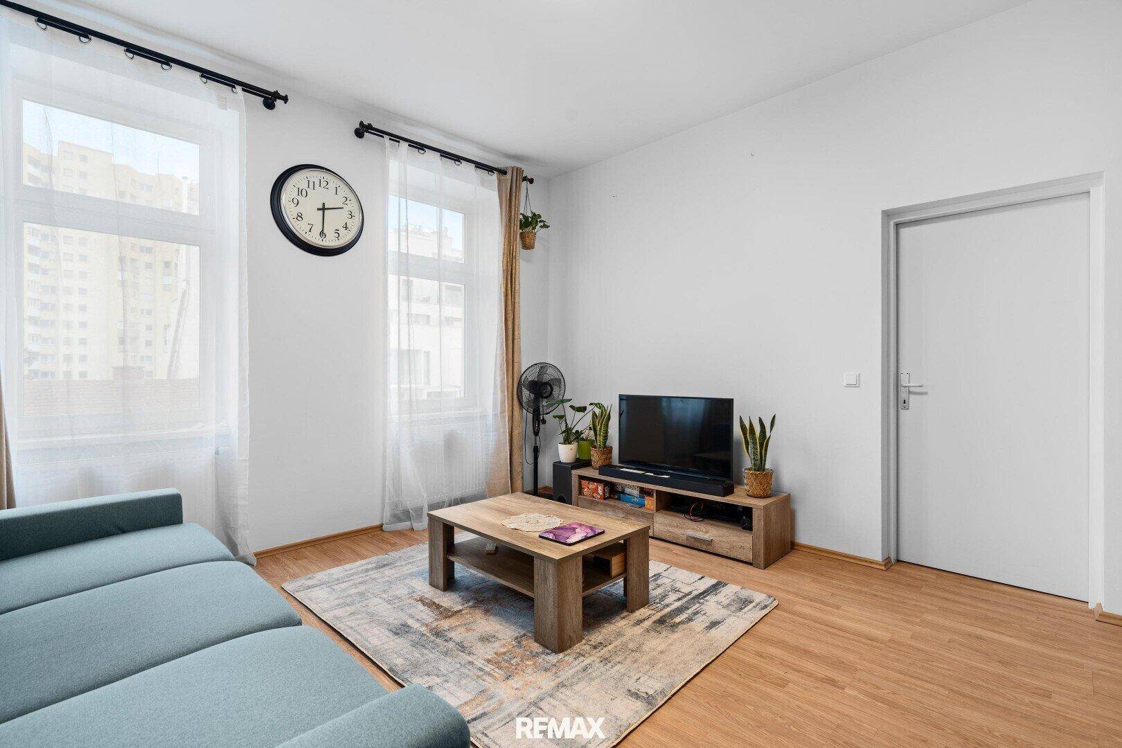 Wohnzimmer mit Holzboden, Fernseher und großem Fenster.