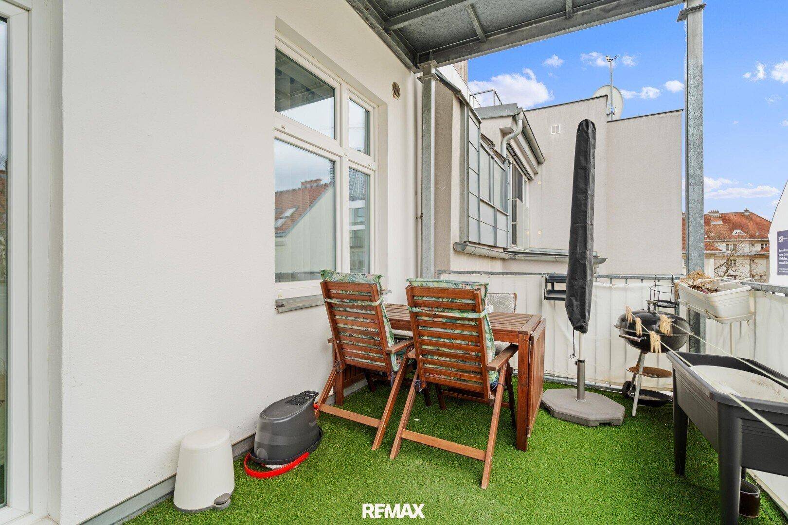 Balkon mit Holztisch, Stühlen und Blick auf die umliegenden Gebäude.