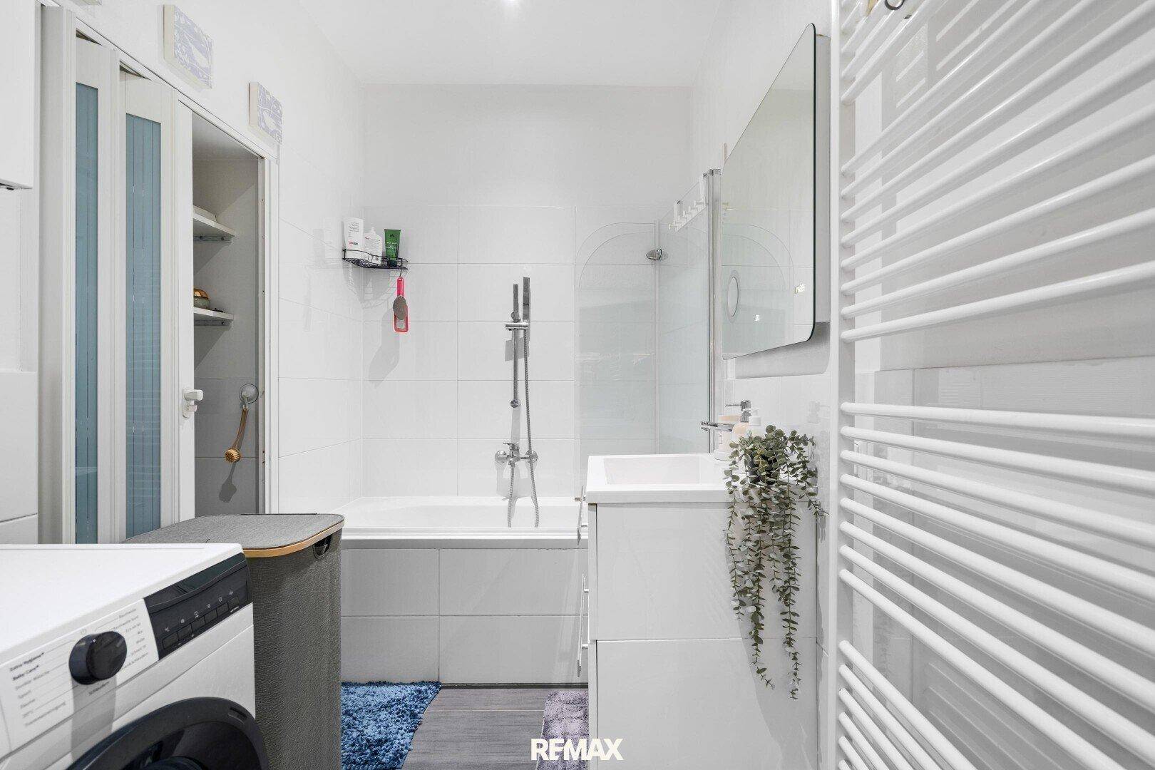 Helles Badezimmer mit Badewanne, Dusche und Waschmaschine.
