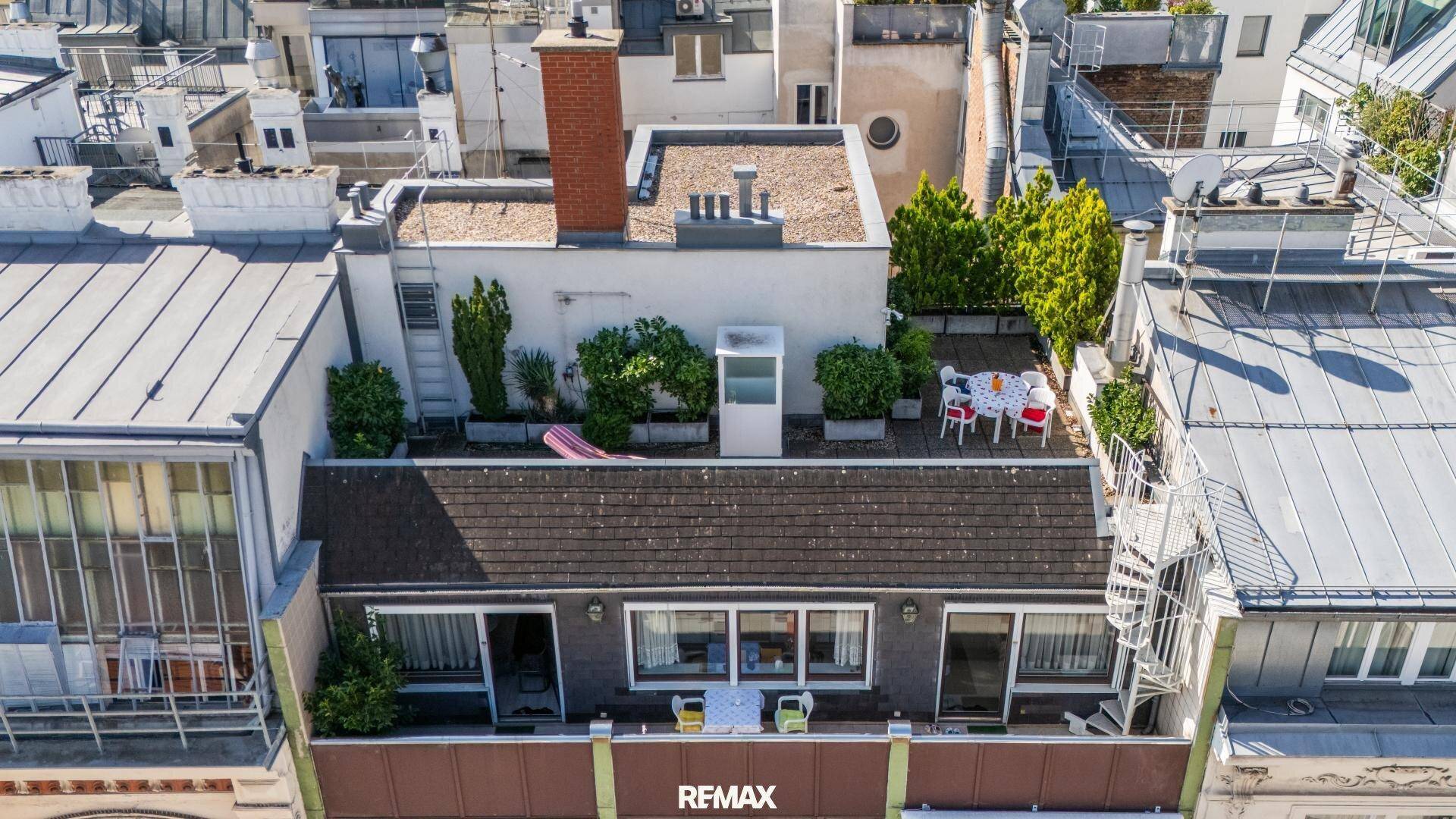 Luftaufnahme eines Gebäudes mit einer möblierten Dachterrasse und umliegenden Dächern der Stadt.