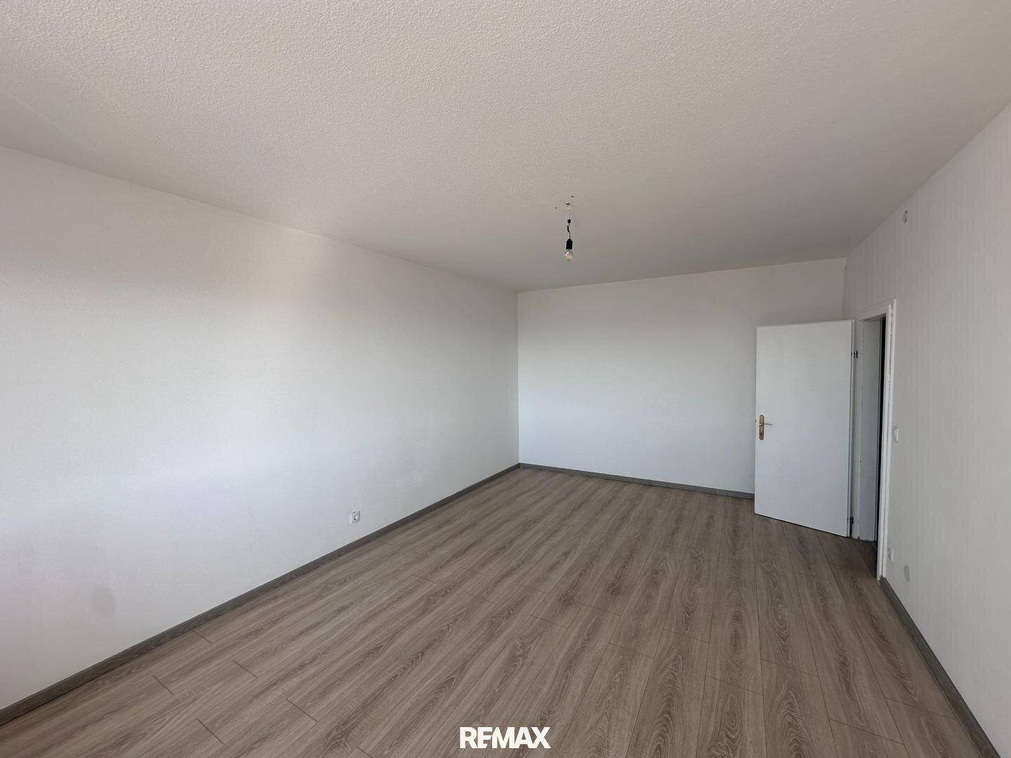 Leeres Zimmer mit hellem Laminatboden und weißen Wänden, bereit zur Einrichtung.