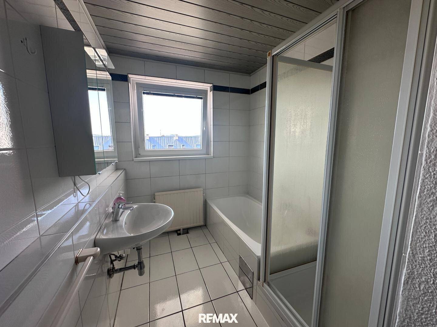 Badezimmer mit Badewanne, Duschabtrennung, Waschbecken und Fenster.