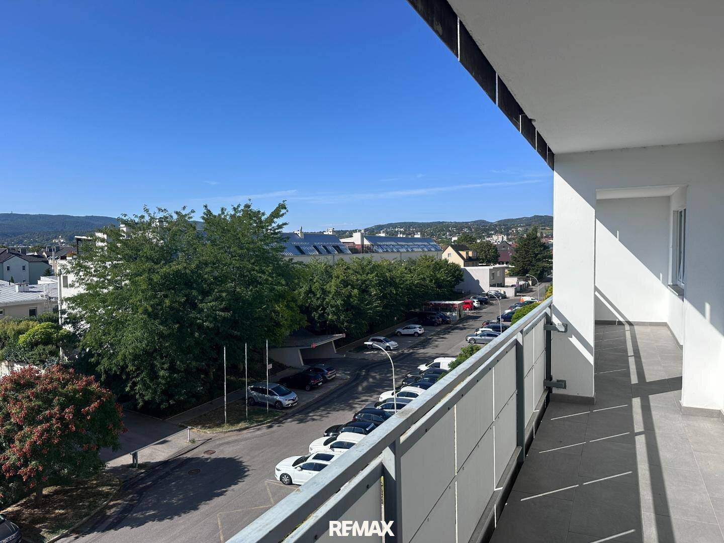 Breiter Balkon mit Stadtblick und umliegenden Gebäuden unter blauem Himmel.