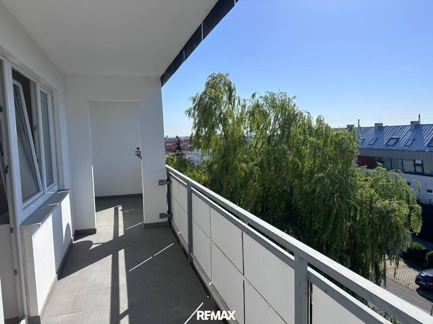 Geräumiger Balkon mit Fliesenboden und Blick auf grüne Bäume an einem sonnigen Tag.