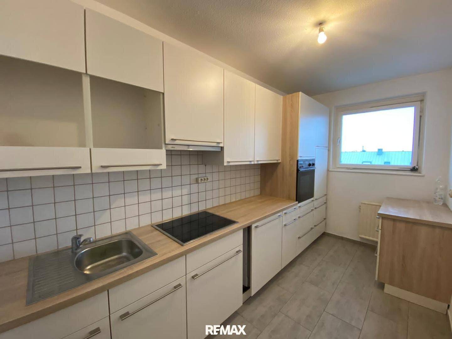 Funktionale Küche mit weißen Schränken, Holz-Arbeitsplatte und Fliesenrückwand.