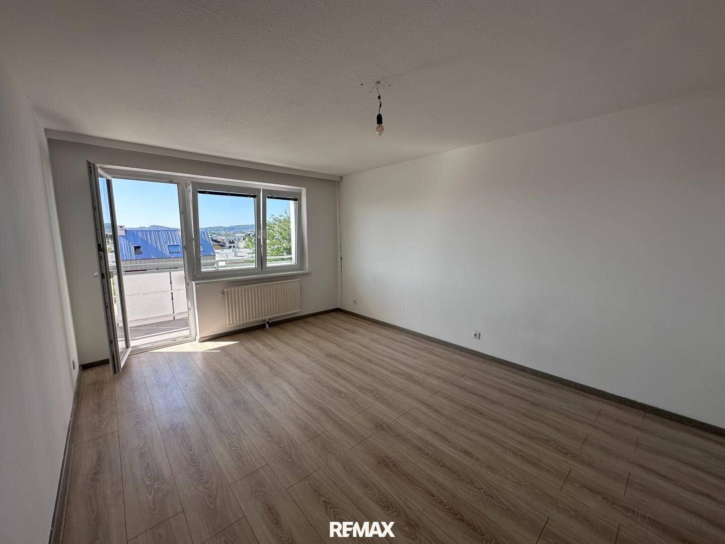 Geräumiges, helles Zimmer mit Laminatboden und Balkonzugang.