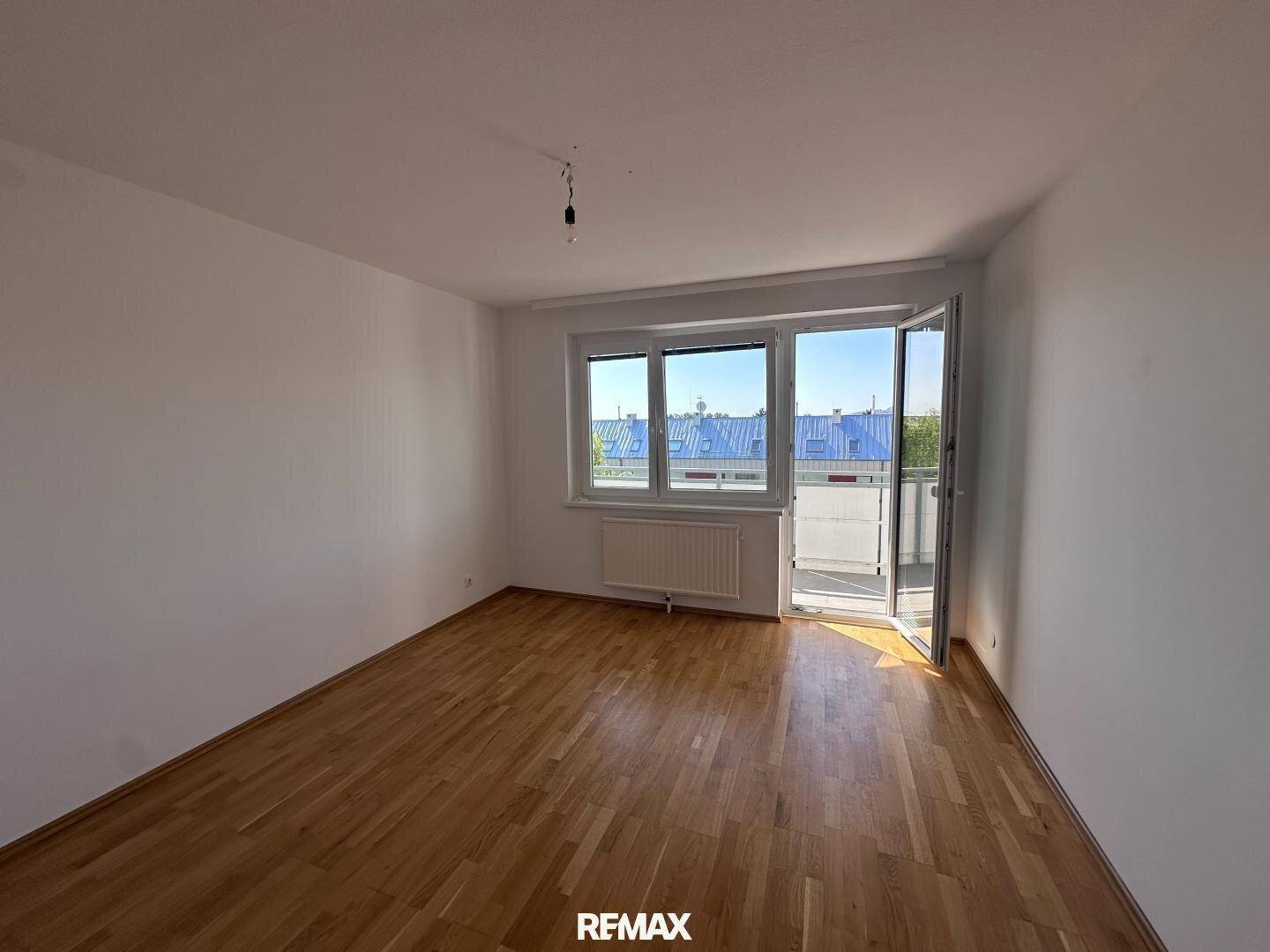 Helles Wohnzimmer mit hellem Parkettboden und Zugang zu einem Balkon.