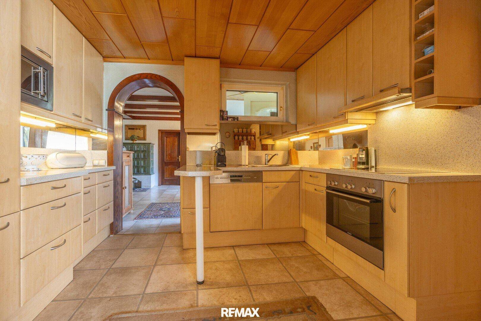 Helle Küche im Landhausstil mit Holzschränken, Fliesenboden und Blick in den Flur.