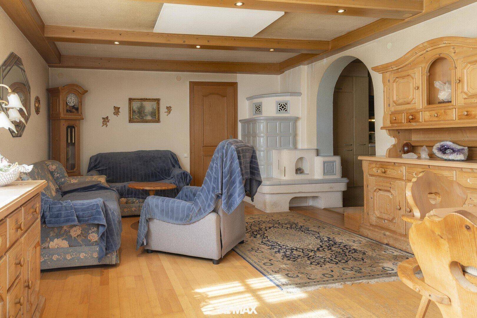Rustikales Wohnzimmer mit Holzboden, Kachelofen und traditionellen Holzmöbeln.