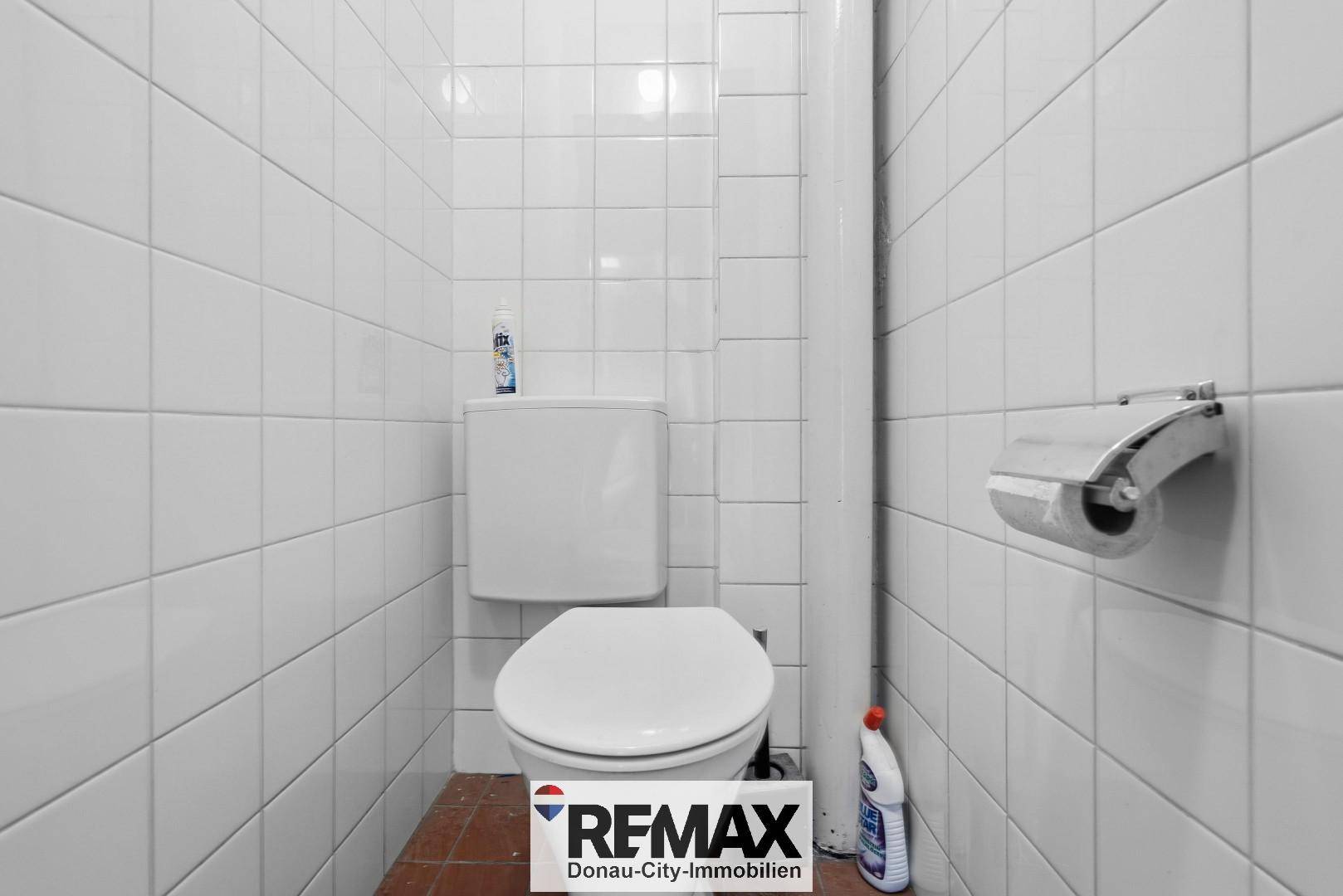 Einfacher Toilettenraum mit weißen Wandfliesen und Terrakotta-Bodenfliesen, sauber und funktional.