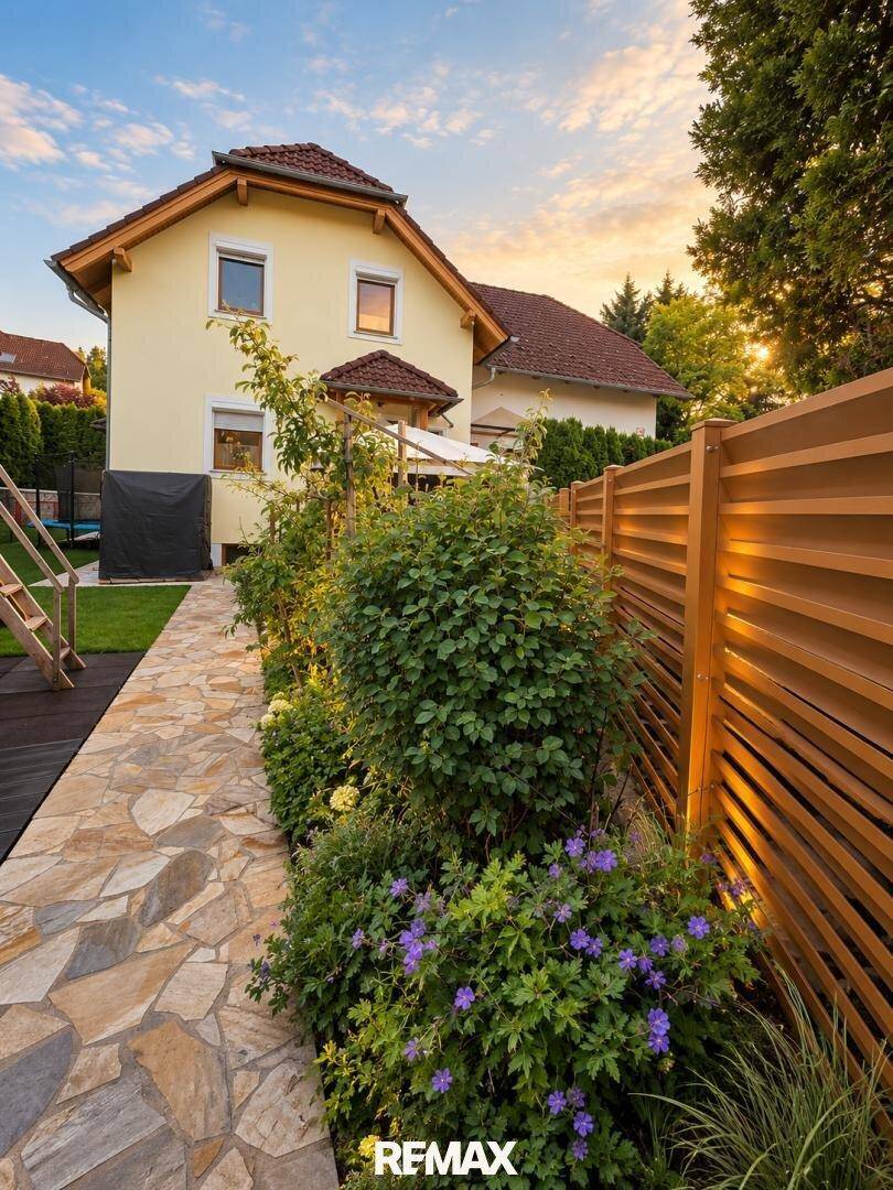 Gepflegter Gartenweg mit Blumenbeeten und Holzzaun, der zum Haus führt.