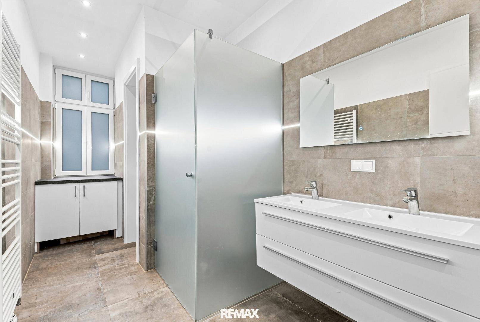 Modernes Badezimmer mit Doppelwaschbecken, großer Dusche und beheiztem Handtuchhalter.