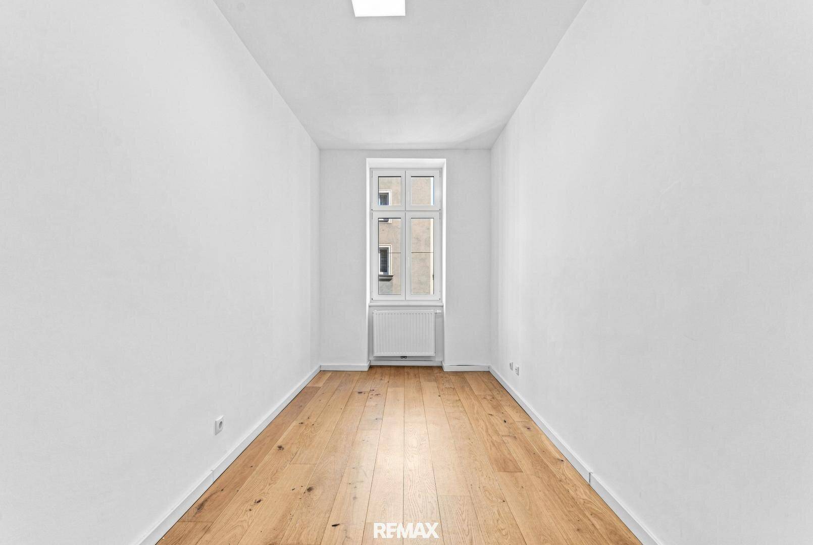 Kleiner, heller Raum mit einem Fenster und Holzboden, geeignet als Kinder- oder Arbeitszimmer.