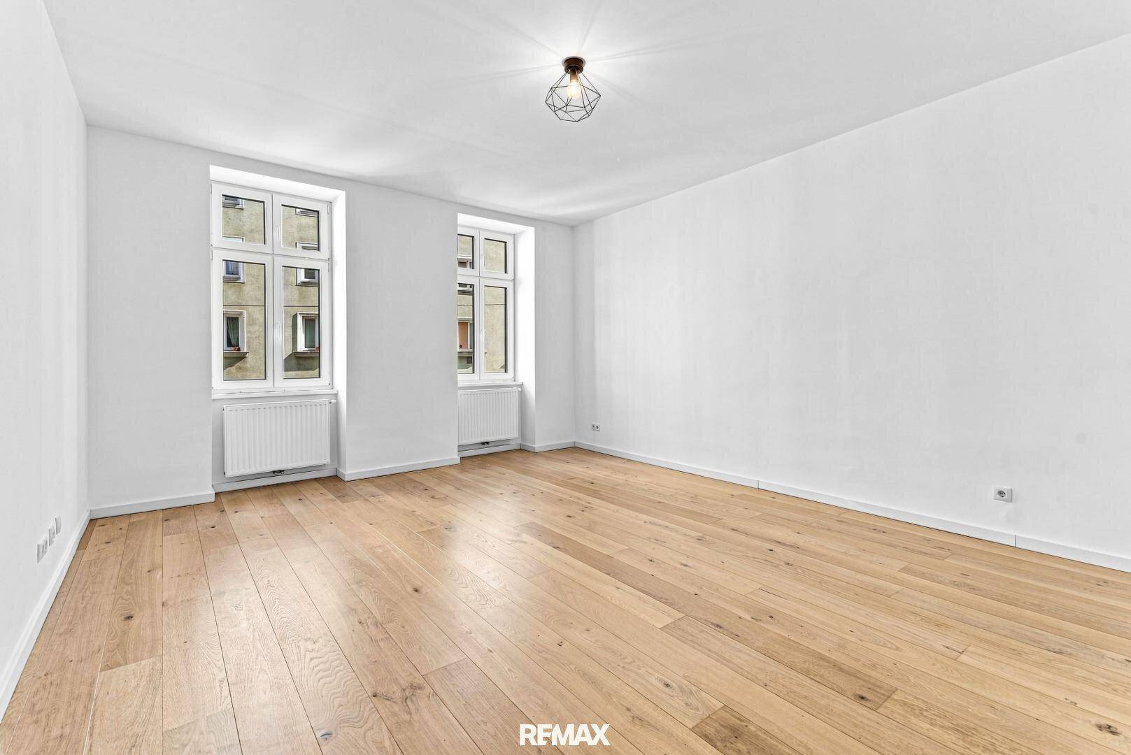 Geräumiger, heller Raum mit zwei Fenstern und Holzboden, ideal als Wohn- oder Schlafzimmer.