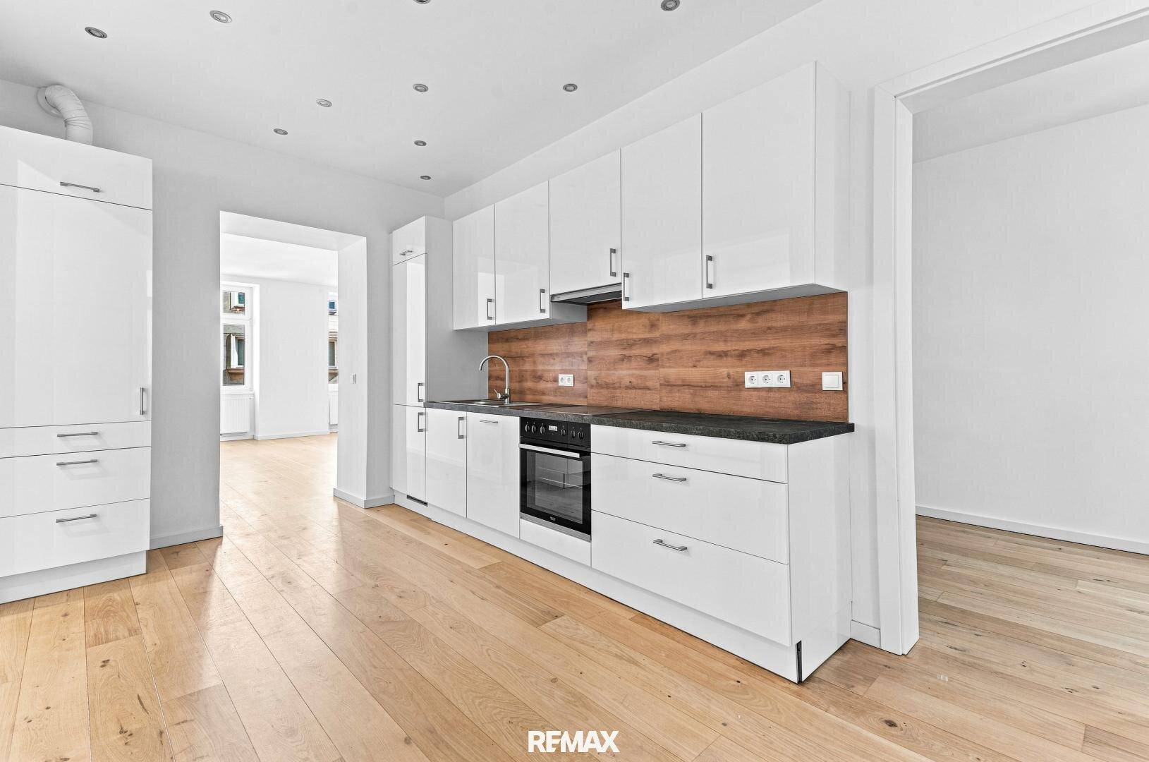 Helle, moderne Küche mit weißen Hochglanzschränken, dunkler Arbeitsplatte und Holzboden.