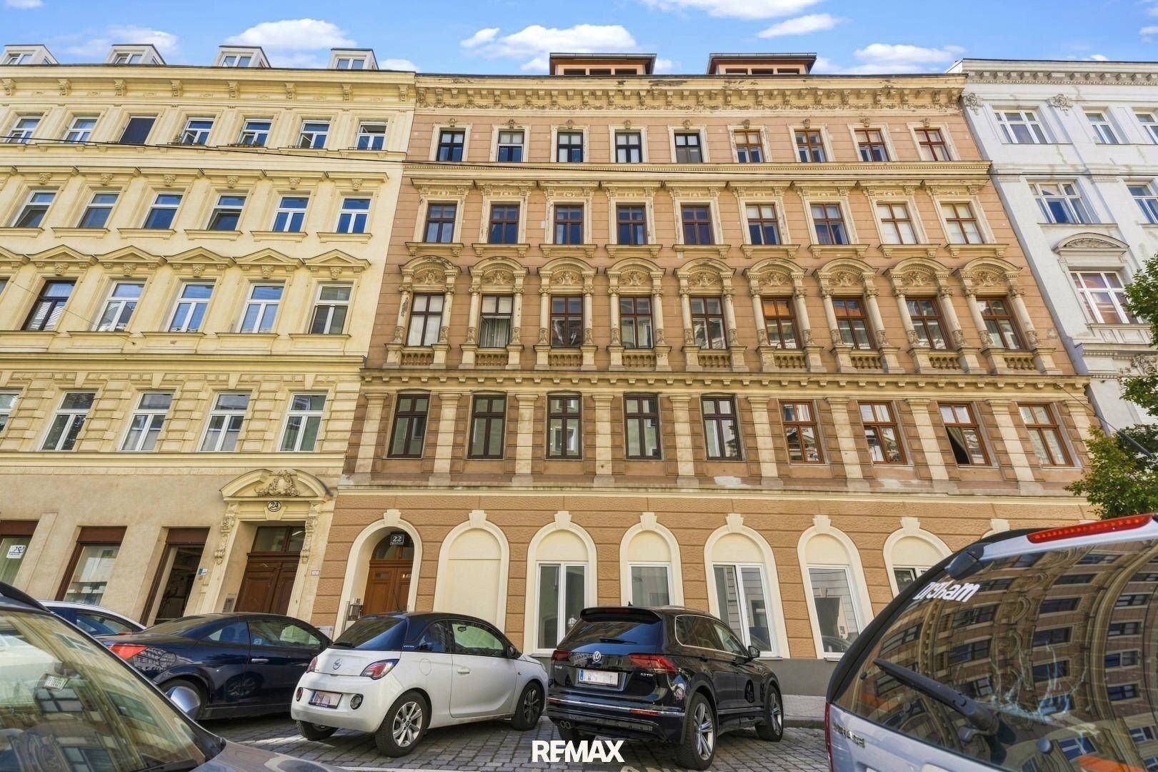 Historische Fassade eines Mehrfamilienhauses mit vielen Fenstern und geparkten Autos davor.