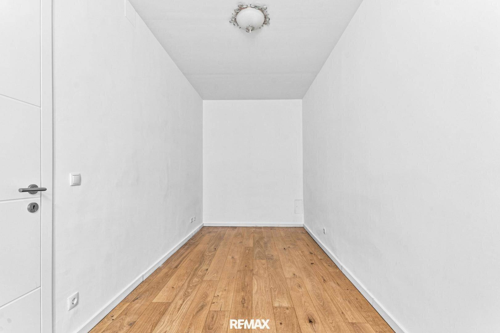 Schmaler, heller Raum mit Holzboden und schlichter Deckenleuchte, vielseitig nutzbar.