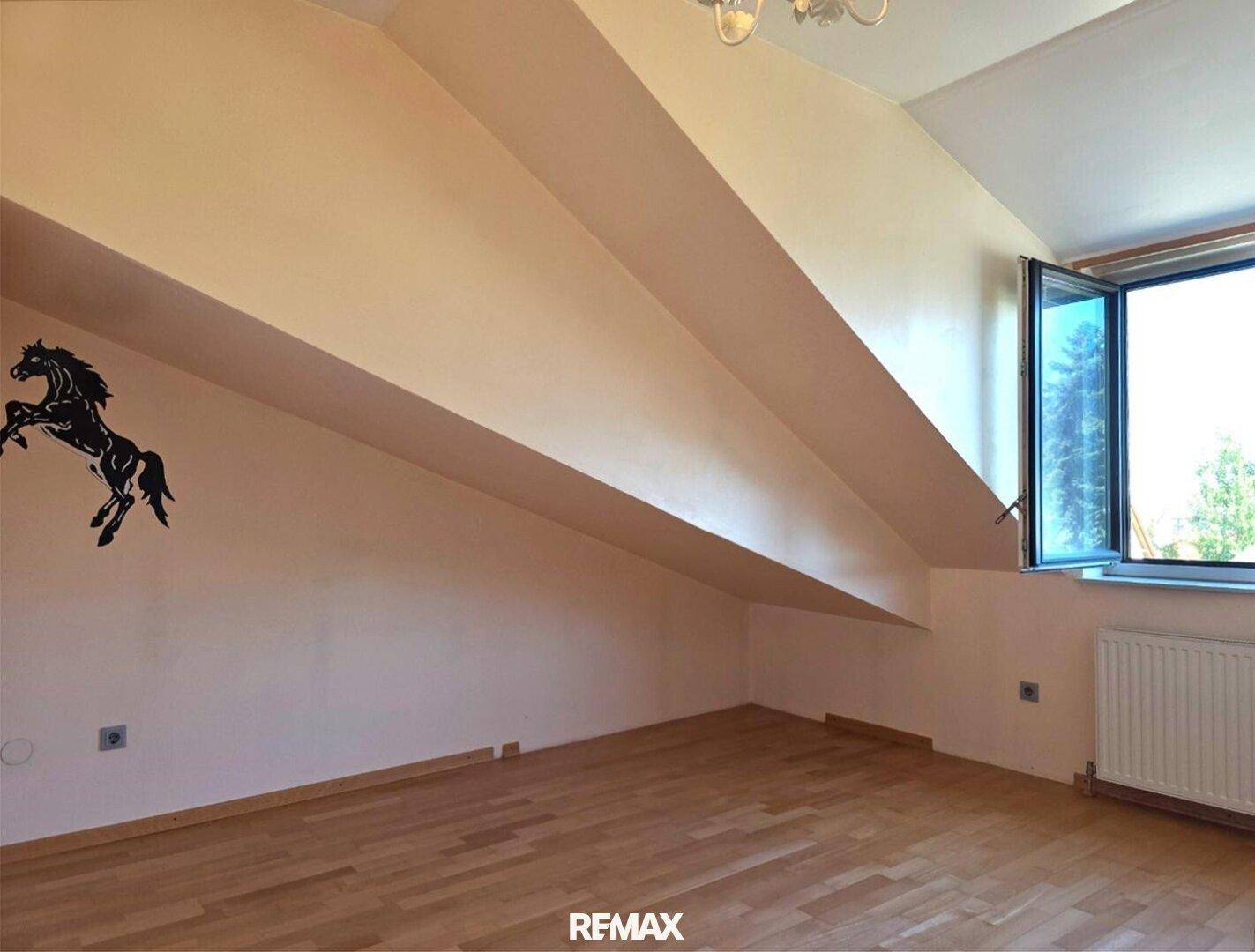 Dachgeschosszimmer mit schrägen Wänden, Holzboden und Fenster.