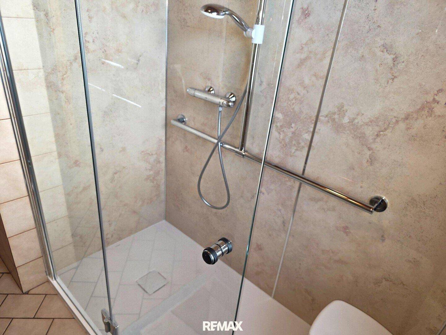Modernisierte Dusche mit Haltegriffen und beigefarbenen Wandfliesen.