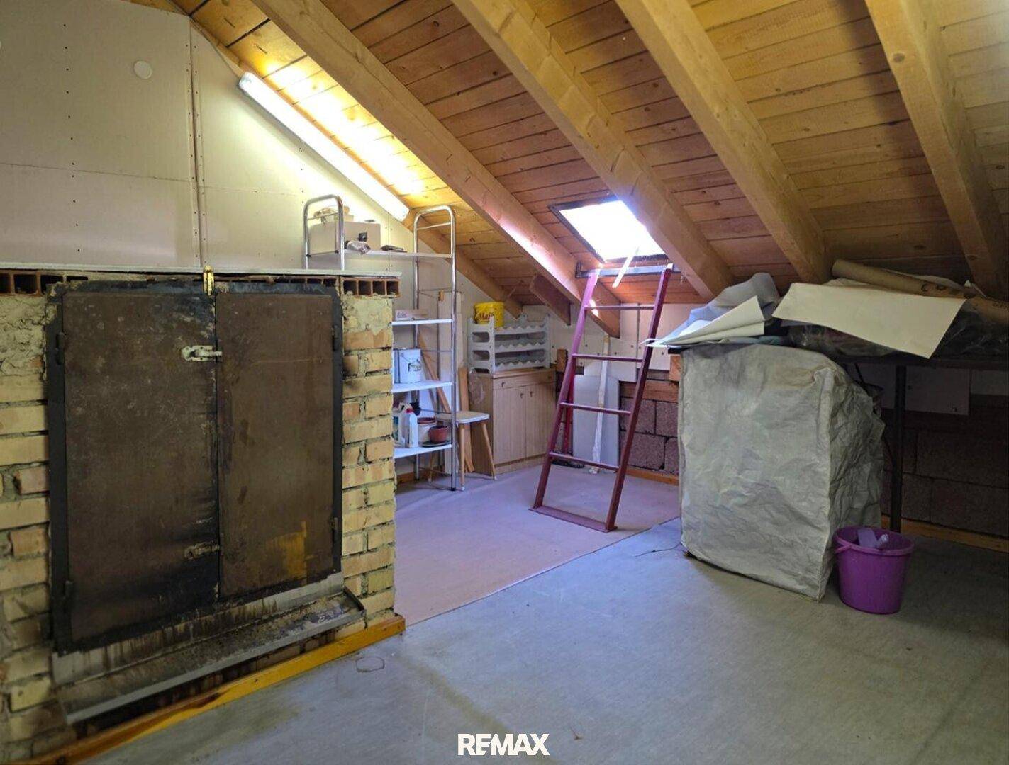 Ausgebauter Dachboden mit sichtbaren Holzbalken und Dachfenster, genutzt als Abstellraum.