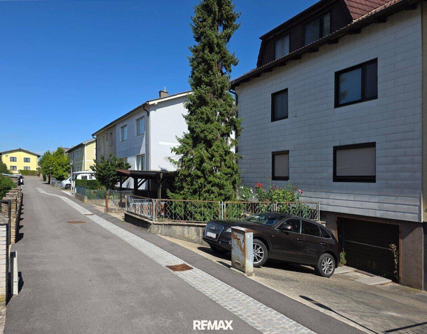 Wohnstraße mit Häusern, geparkten Autos und einer Garage an der Seite des Gebäudes.