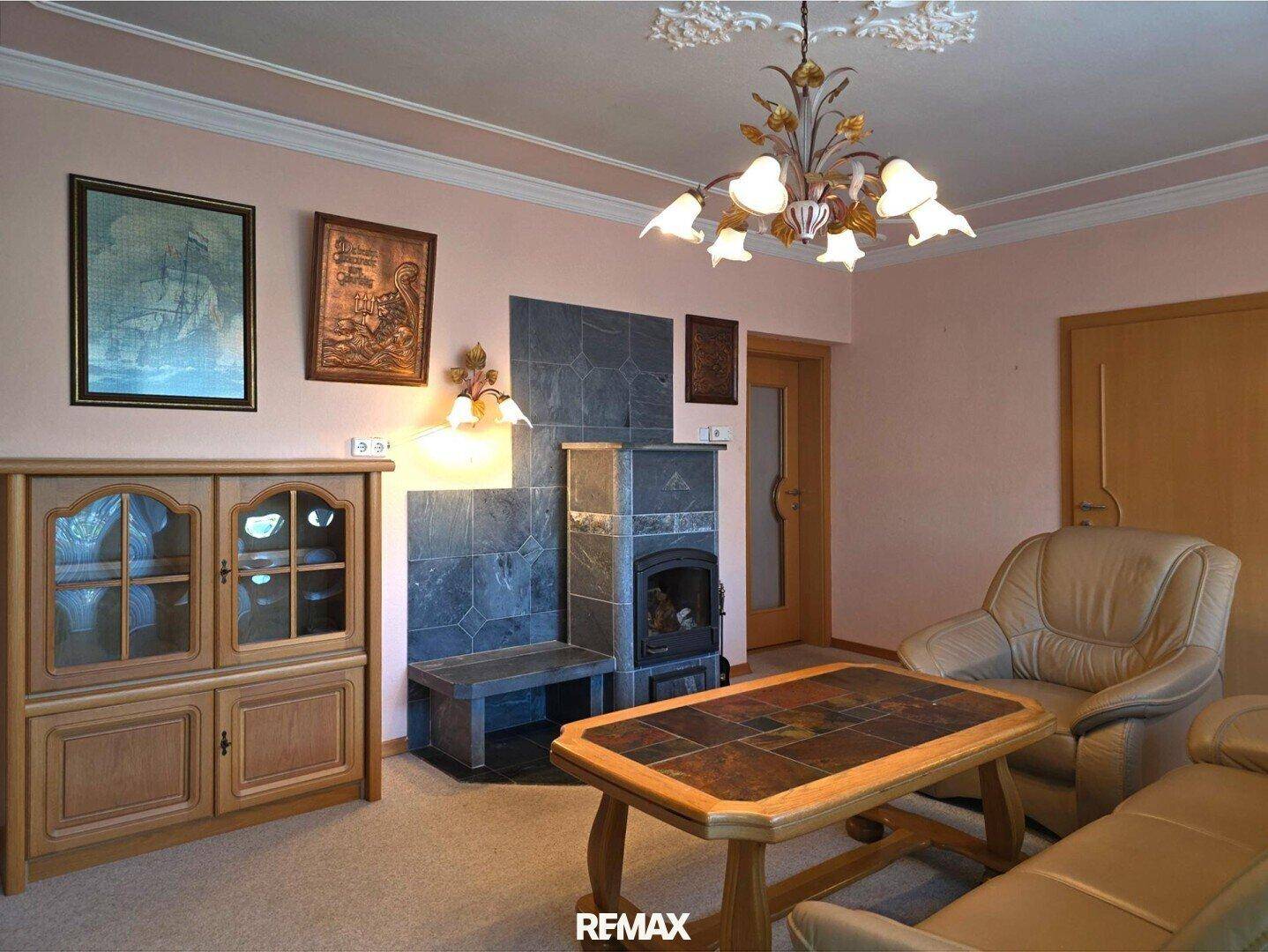 Gemütliches Wohnzimmer mit Kachelofen, Stuckdecke und bequemen Ledersofas.