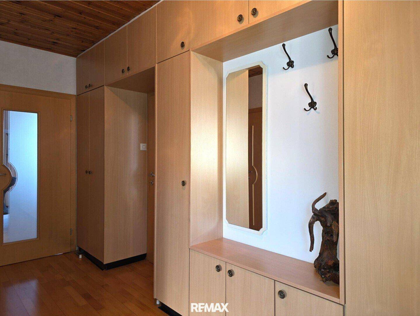 Flur mit Einbauschränken aus hellem Holz und einem Spiegel, der viel Stauraum bietet.