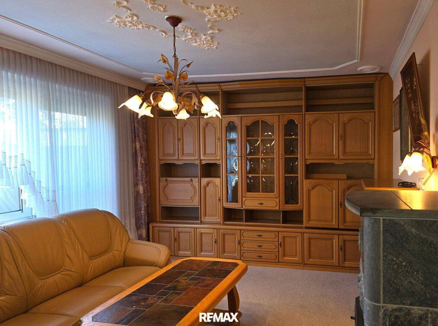 Wohnzimmer mit großer Holzschrankwand, Teppichboden und traditioneller Deckenleuchte.