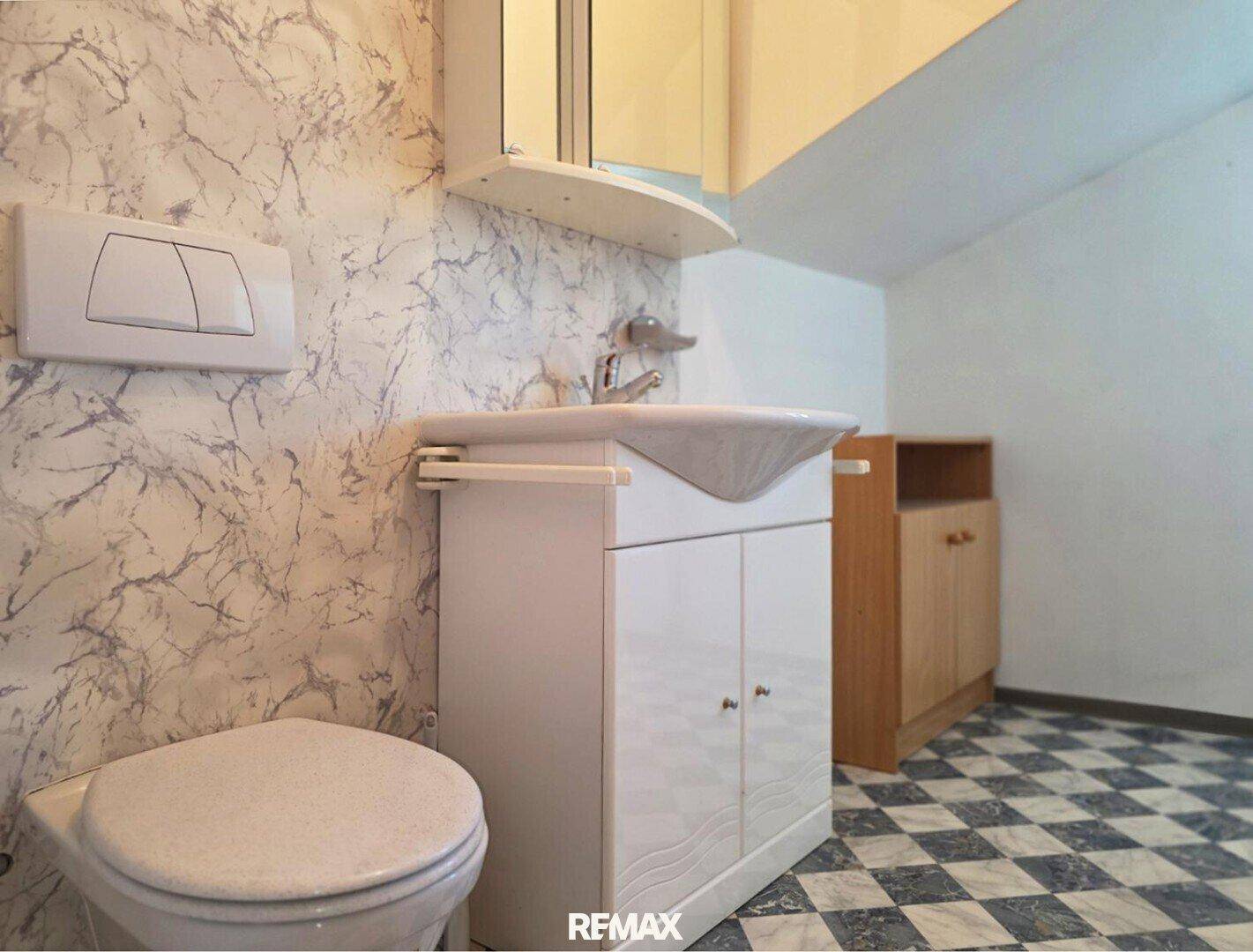 Badezimmer im Dachgeschoss mit WC, Waschbecken und gemustertem Fliesenboden.