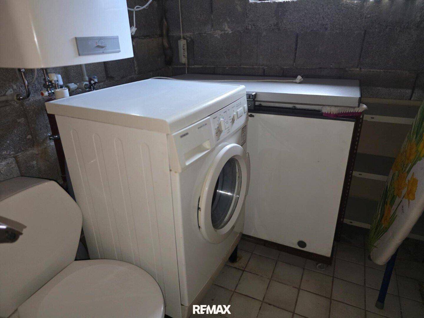 Kleiner WC-Bereich im Keller mit Toilette, Waschmaschine und Warmwasserboiler.