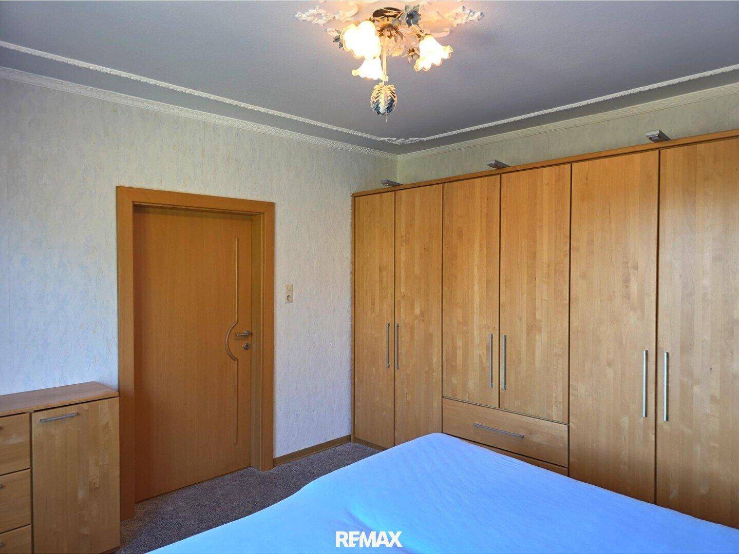 Schlafzimmer mit großem Kleiderschrank aus hellem Holz und Teppichboden.