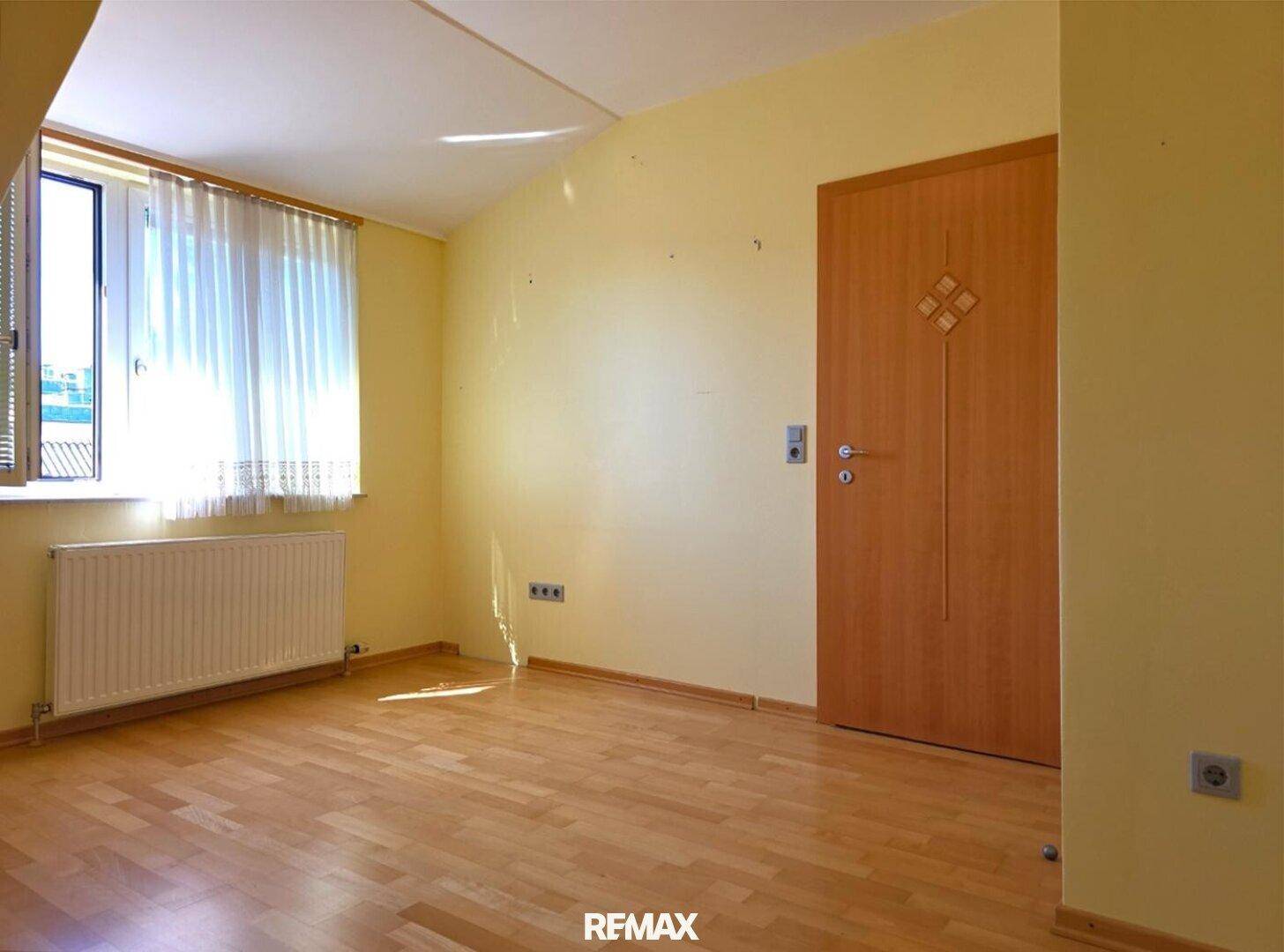 Helles Zimmer mit Holzfußboden und Fenster, das viel Tageslicht hereinlässt.