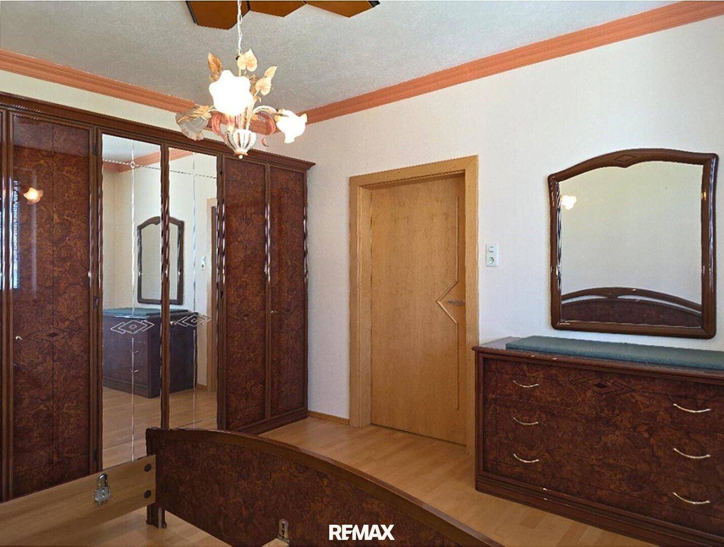 Schlafzimmer mit dunklen Holzmöbeln, Spiegelschrank und Parkettboden.