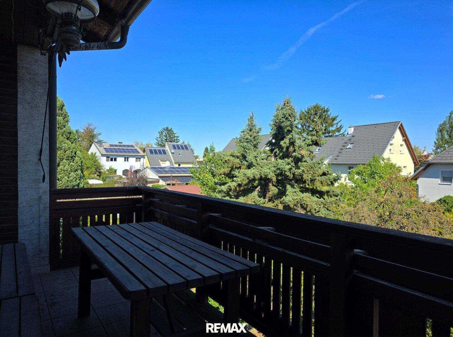 Balkon mit Holztisch und Blick auf die umliegenden Häuser und grüne Landschaft.