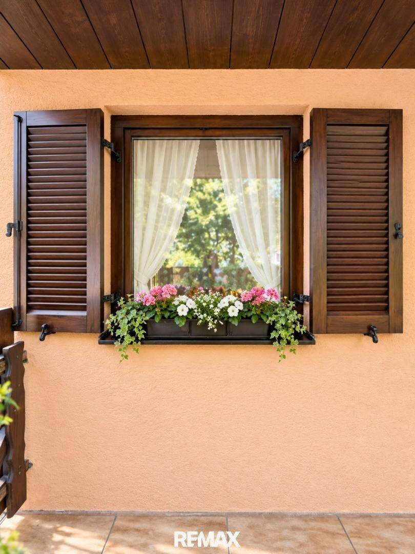 Fenster mit geöffneten Holzläden und bunten Blumenkästen, die das Haus schmücken.