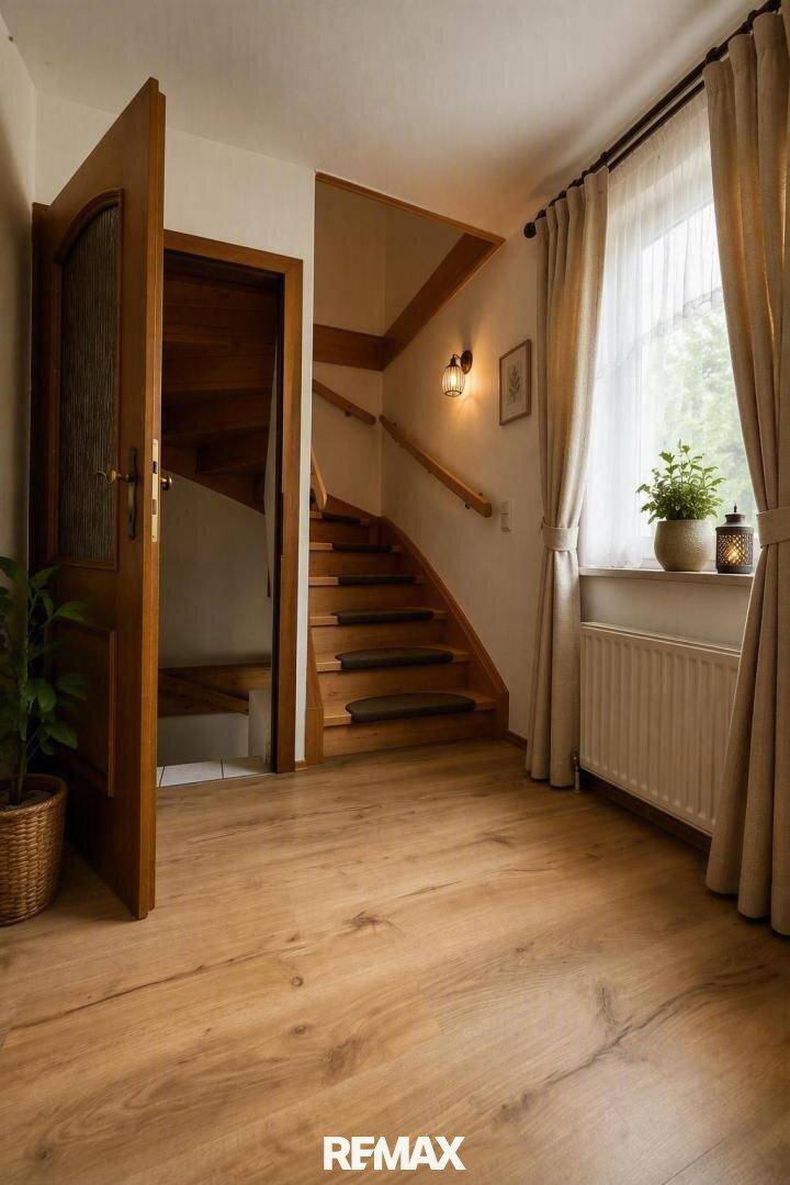 Heller Flur mit Holztreppe, Parkettboden und Fenster mit Vorhängen.