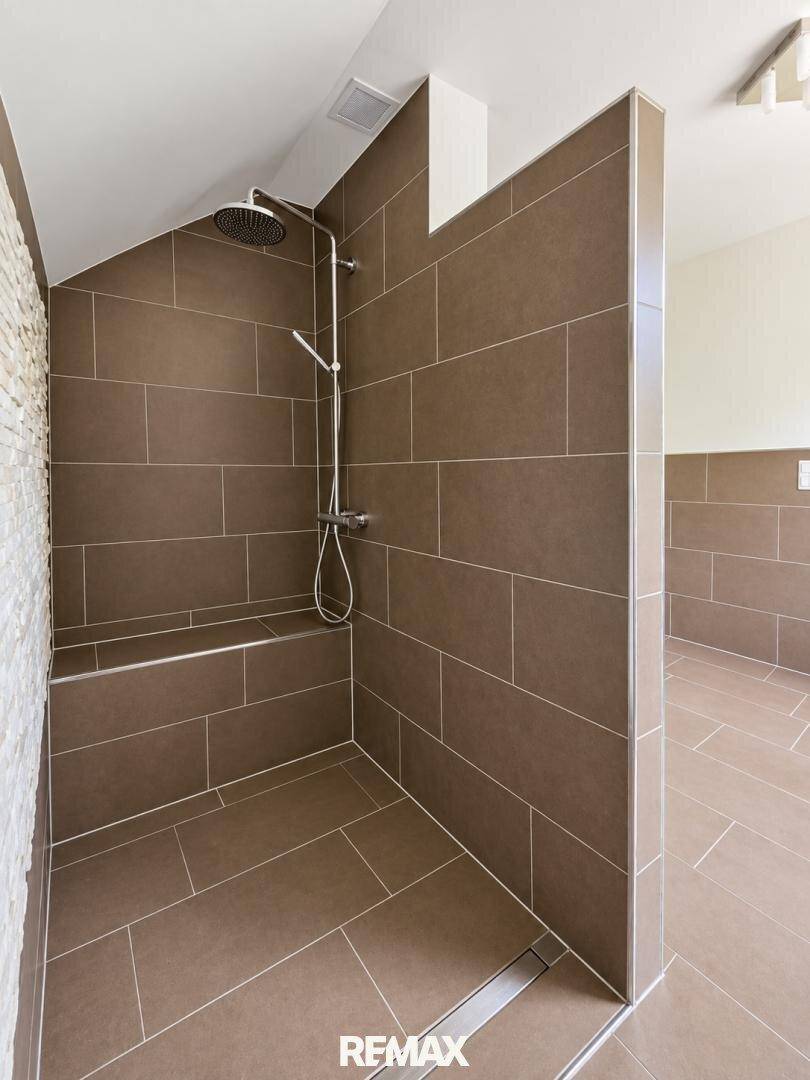 Geräumige begehbare Dusche mit braunen Fliesen und Dachschräge.