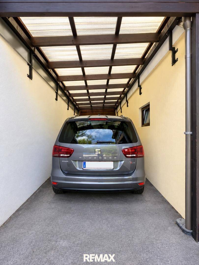 Überdachter Stellplatz für ein Fahrzeug, geschützt unter einem Carport mit Holzbalken.
