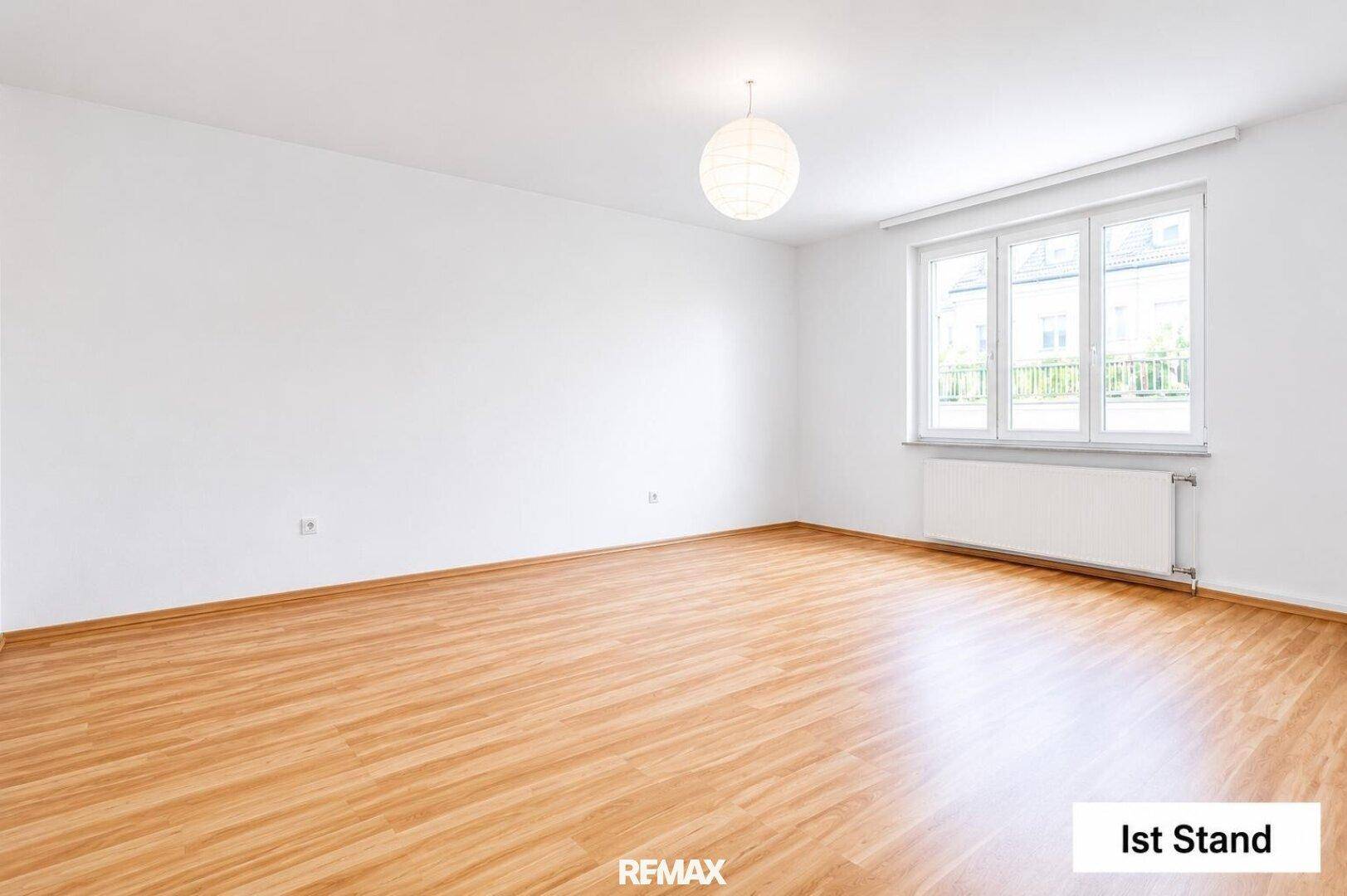 Leerer Wohnraum mit hellem Laminatboden und großen Fenstern, bereit zur individuellen Gestaltung.