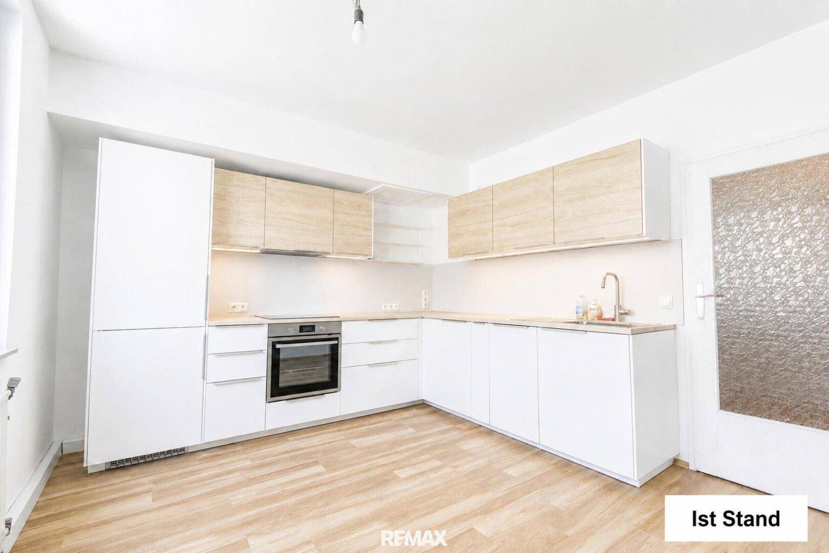 Leere Küche mit weißen und holzfarbenen Einbauschränken und hellem Laminatboden.