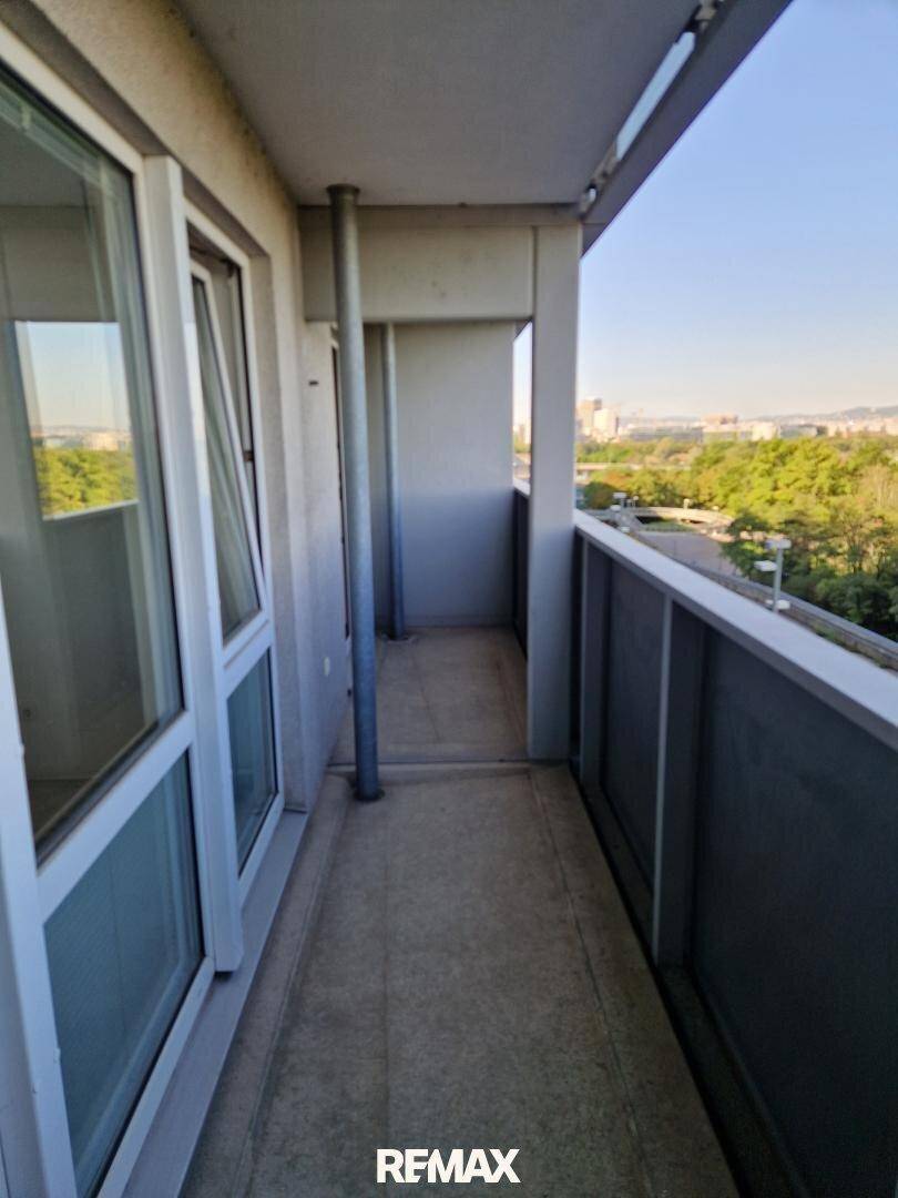 Schmaler Balkon mit Betonboden und Blick auf grüne Bäume und die Stadtlandschaft.