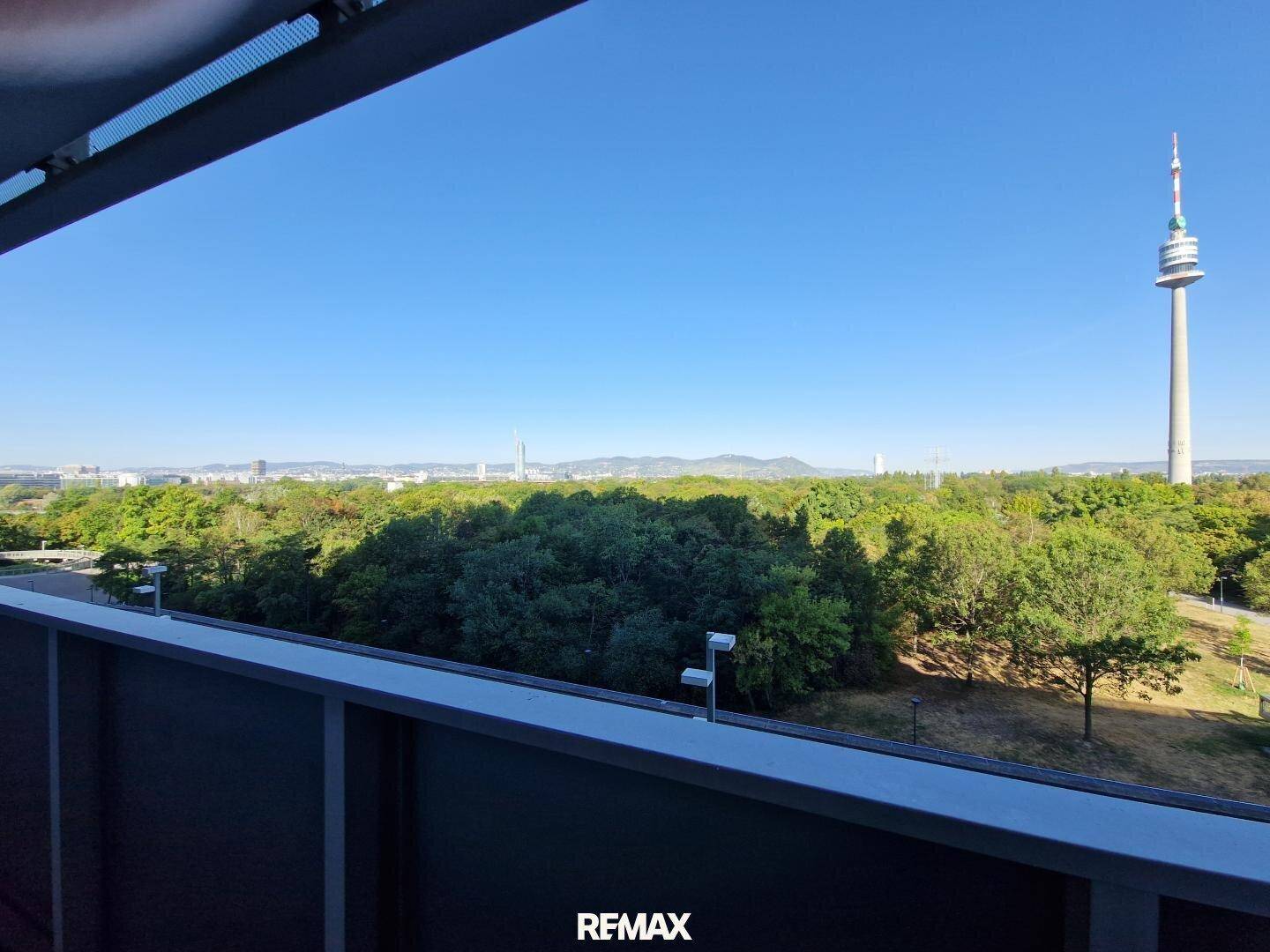 Panoramablick vom Balkon auf den Donauturm, weite Grünflächen und die beeindruckende Stadtsilhouette.