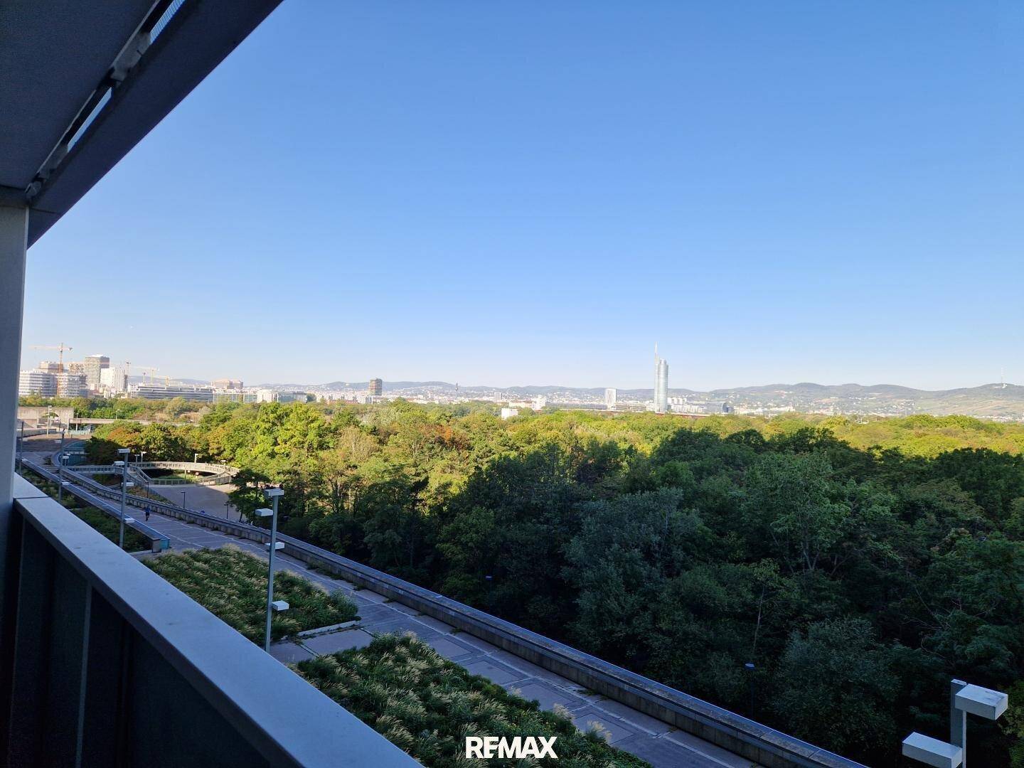 Weitläufiger Ausblick vom Balkon über grüne Baumwipfel, eine Straße und die Skyline der Stadt.