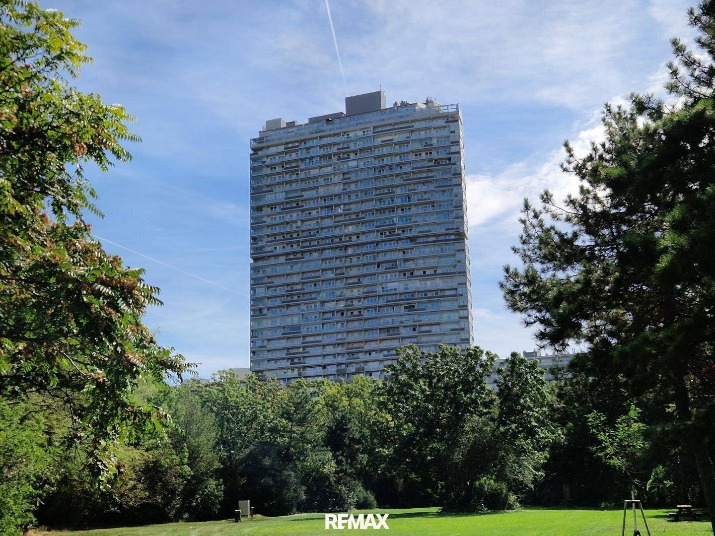 Hohes modernes Wohngebäude umgeben von üppigen Grünflächen unter strahlend blauem Himmel.