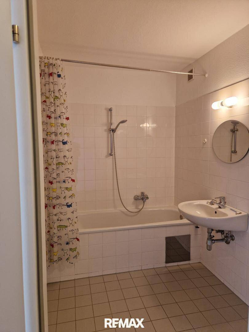Badezimmer mit weiß gefliesten Wänden, Badewanne mit Duschfunktion und einem Waschbecken.