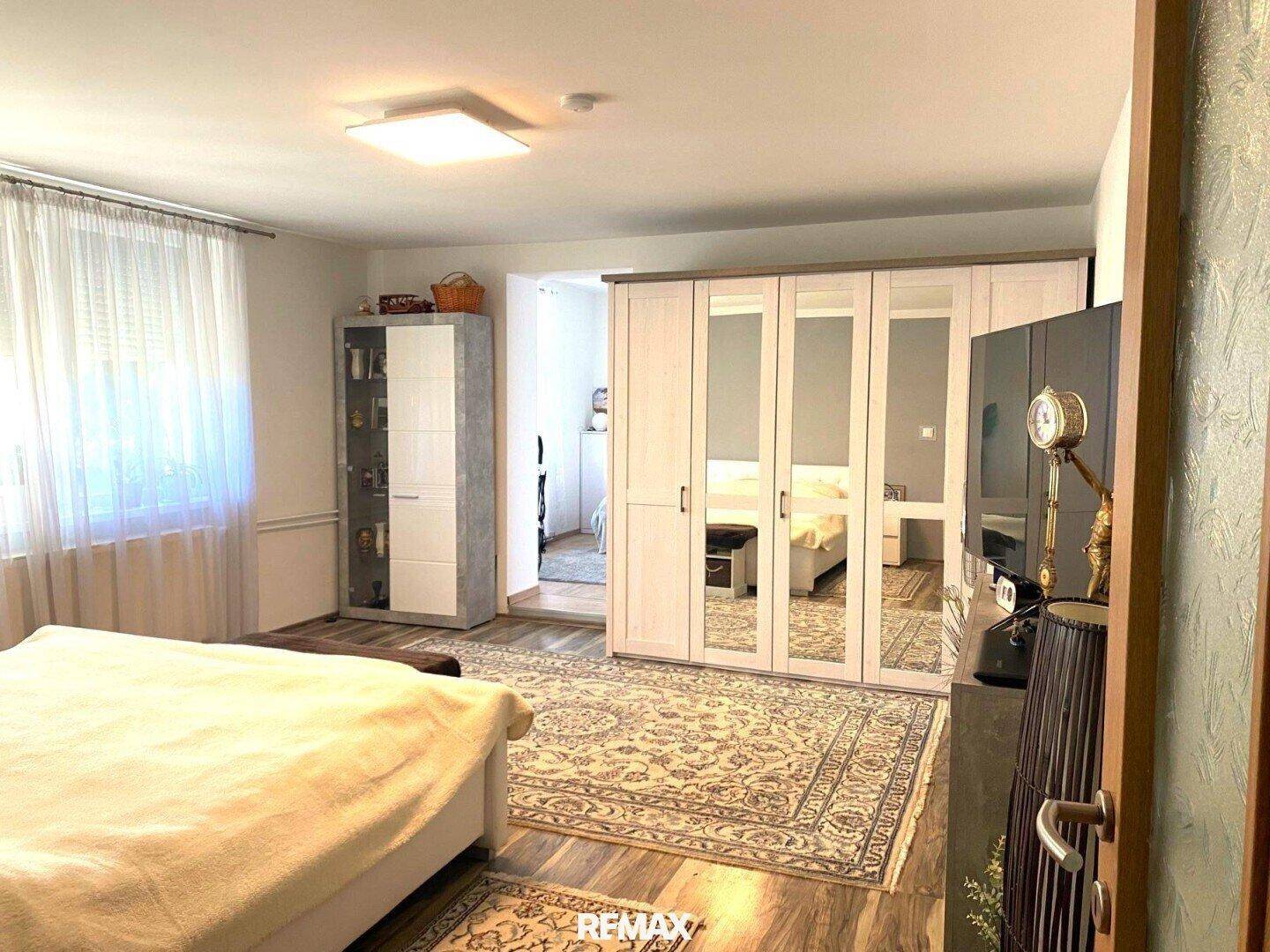 Helles Schlafzimmer mit großem Bett, Spiegelschrank und Holzfußboden, bietet viel Stauraum.